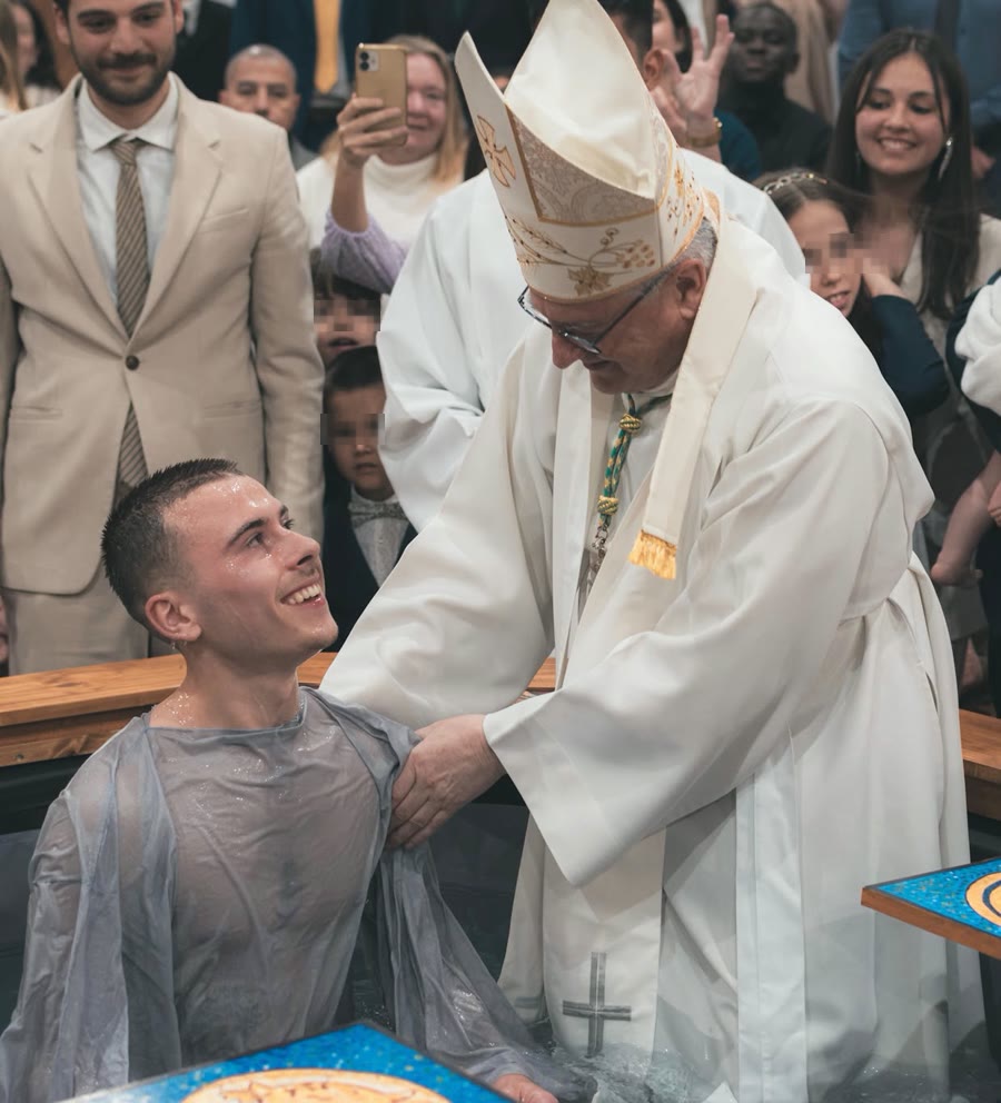 Un adulte, tout juste baptisé, sourit à l'évêque qui l'accueille au sortir de la cuve baptismale