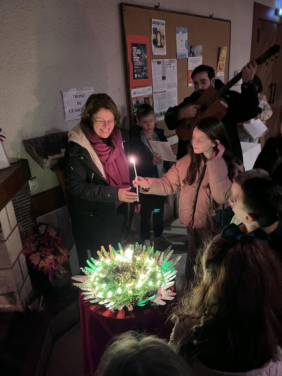 Une catéchiste et des enfants allument une bougie de la couronne de l'Avent, accompagnés à la guitare