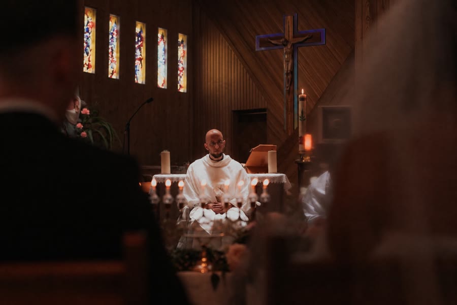 Le prêtre assis devant l'autel pendant une célébration de mariage, les mariés de dos au premier plan